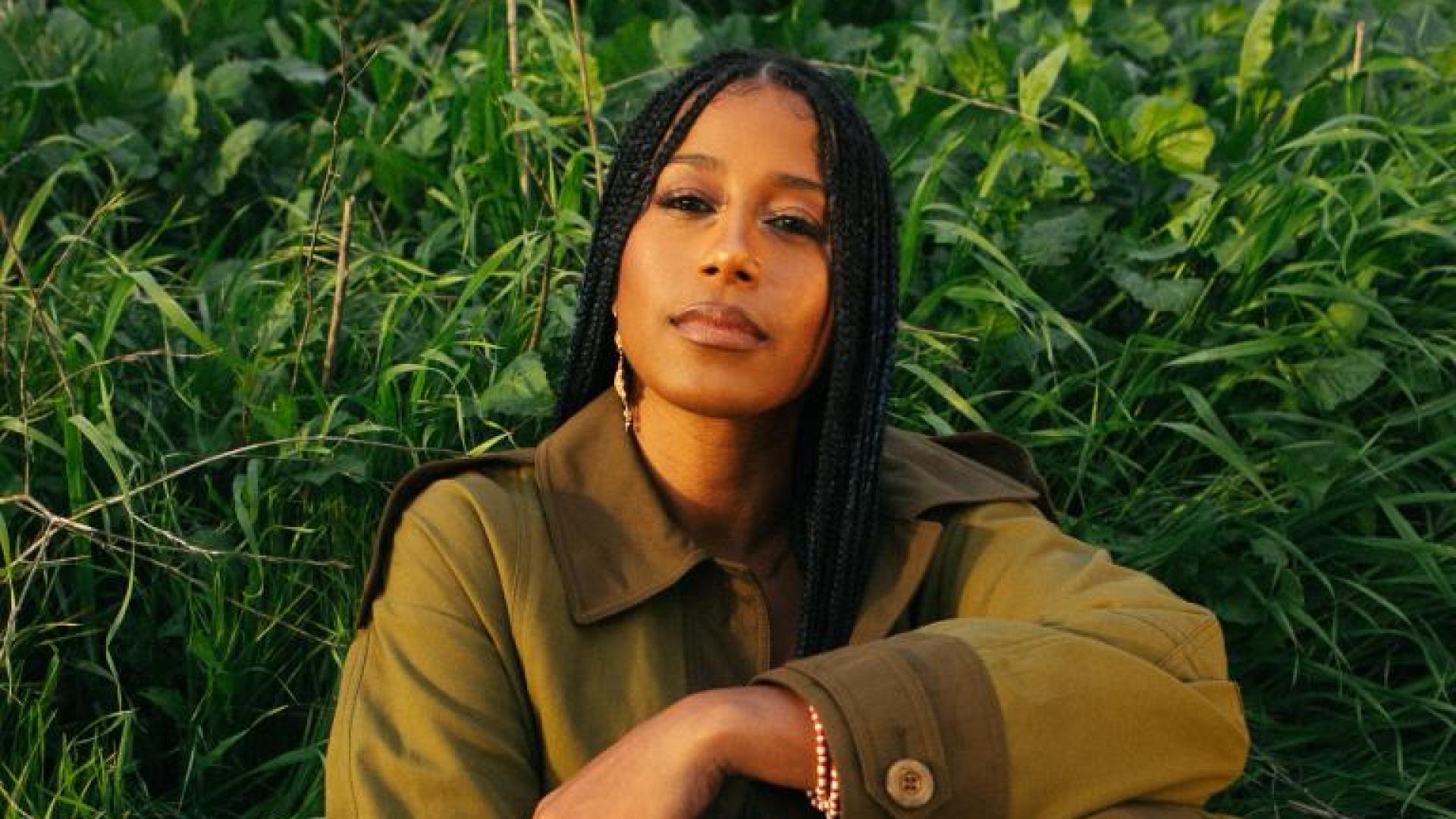 aja monet sitting in the grass with her arm across her knee