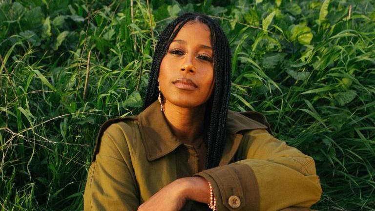 aja monet sitting in the grass with her arm across her knee
